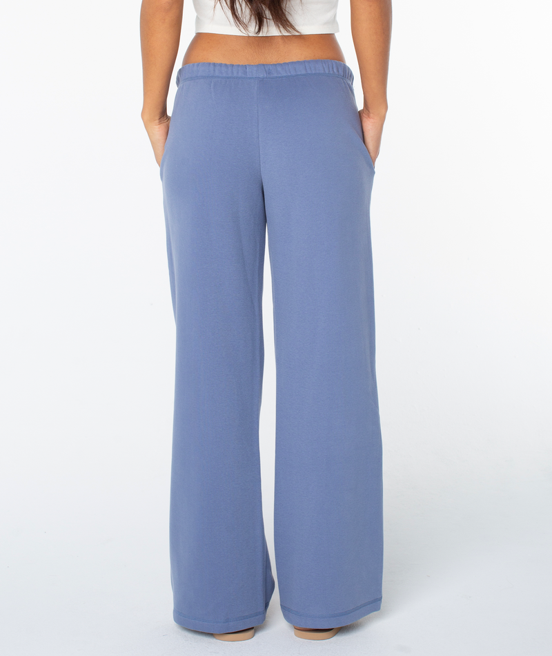 A person wearing loose-fitting, high-waisted Ariel Wide Leg Pant by Roxy, made from a soft cotton blend with side pockets and an elastic waistband, viewed from the back.