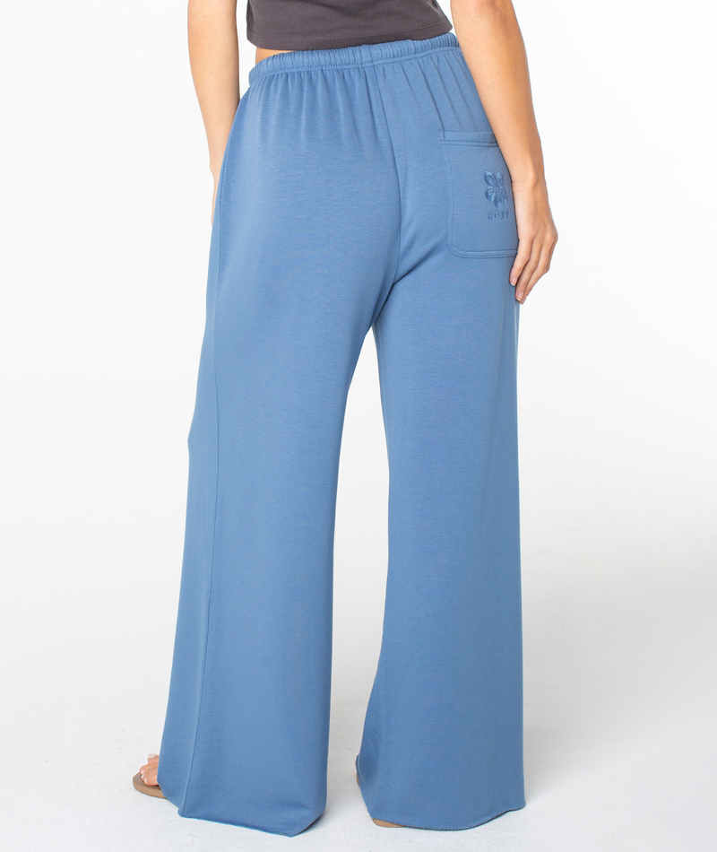 A person seen from behind wears the Roxy Surfing By Moonlight Pant—high-waisted, wide-leg lounge pants with a back pocket and flattering fit—paired with a dark top.