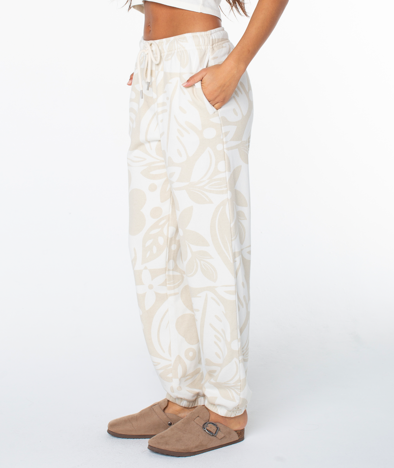 Person wearing cream-colored Roxy Maile Printed Pants with a light brown leaf pattern, featuring an elastic drawstring waist and side pockets.