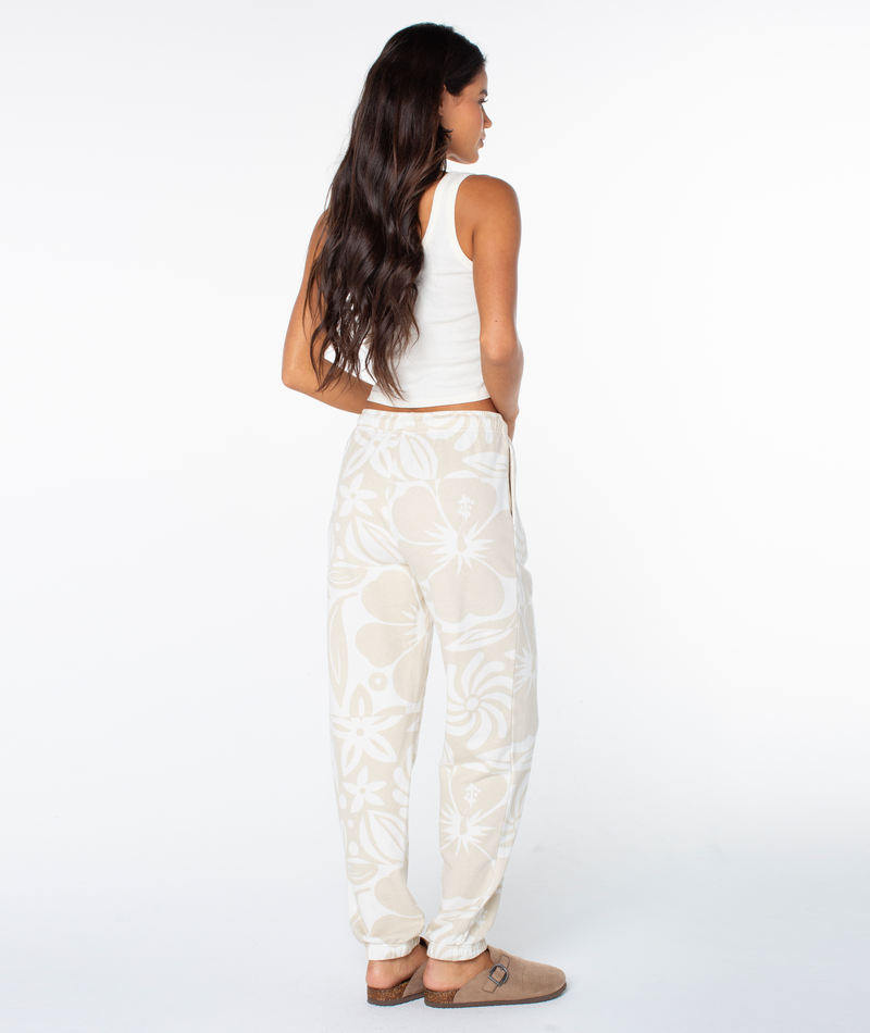 A person seen from behind wears a white tank top and Roxy Maile Printed Pant with bold florals, paired with tan slide sandals.