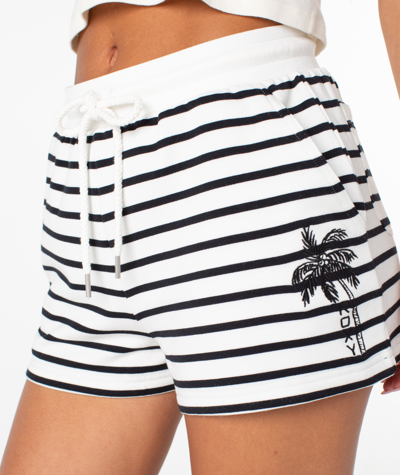 A person wears the Roxy Surfing By Moonlight Stripe Short, featuring black horizontal stripes, a drawstring waistband, and a small palm tree graphic on the left side. These beach shorts are crafted from soft modal stretch fabric for added comfort. The background is plain white.