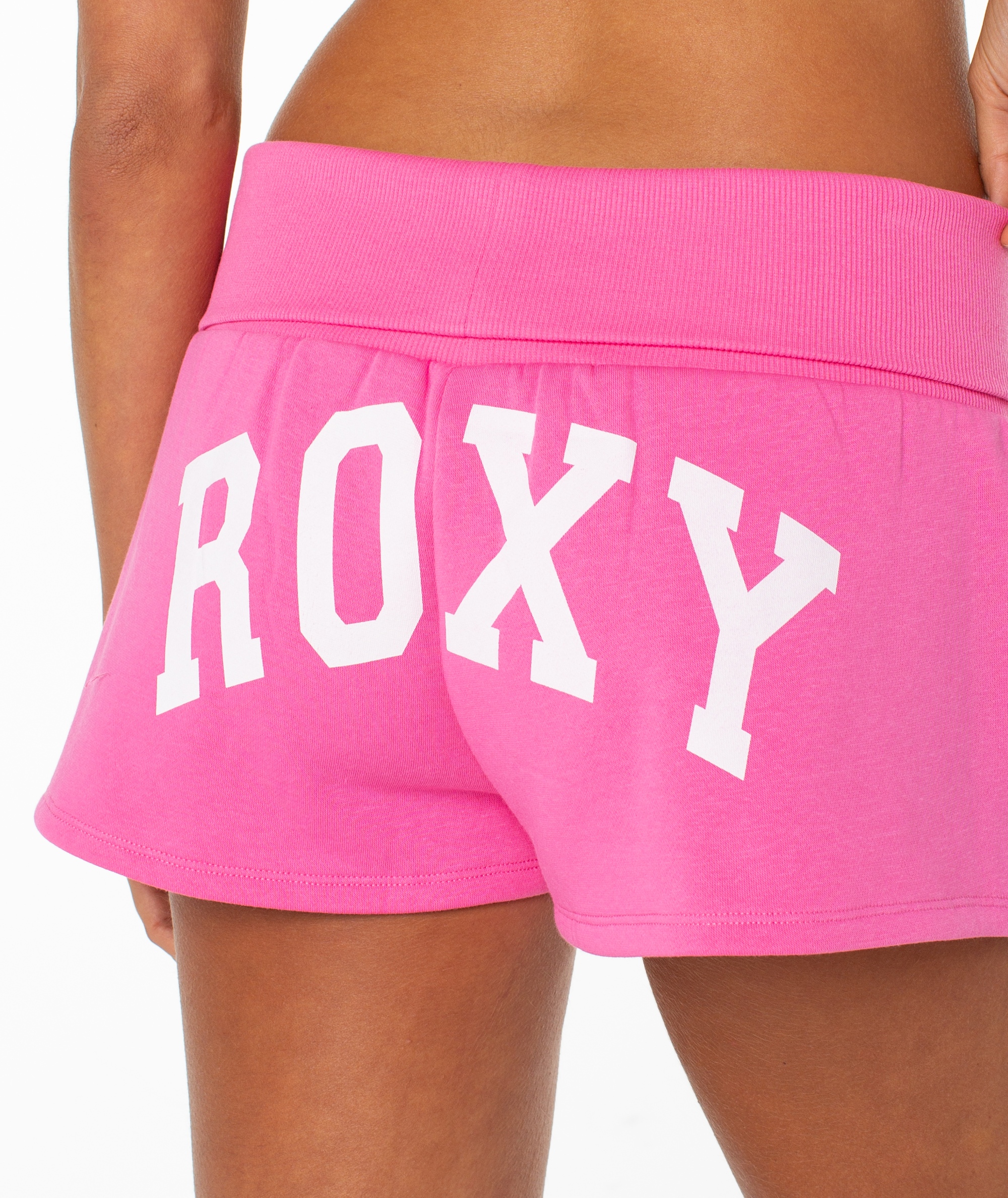 Close-up of a person wearing the Roxy Sunday Short in bright pink, featuring large white "ROXY" lettering on the back and a comfy cotton blend fold-over waistband.
