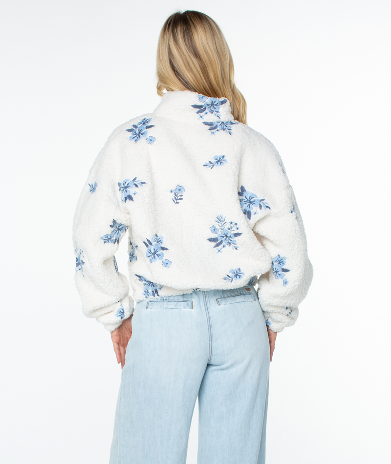 Back view of a cream-colored, fuzzy fleece Roxy Cold Surf Fleece Top with a blue floral pattern, a stand-up collar, and a relaxed silhouette.