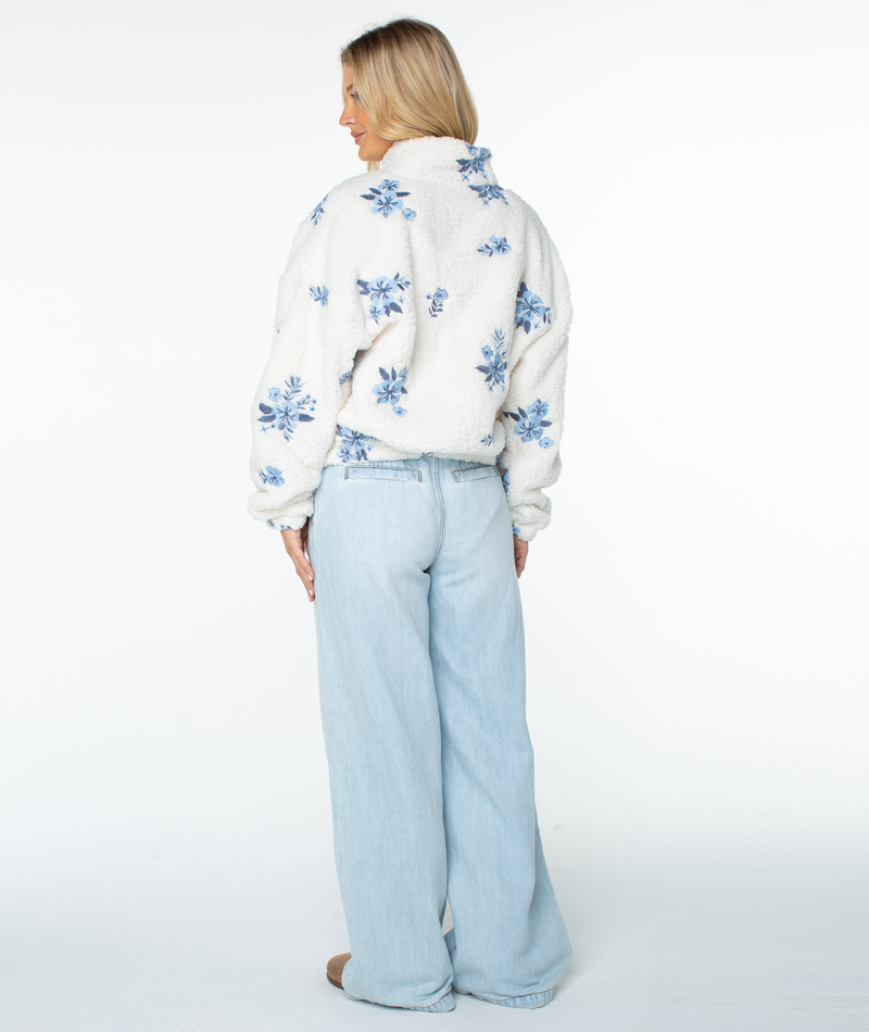 A person seen from behind in a relaxed-silhouette white, fuzzy fleece Roxy Cold Surf Fleece Top with a blue floral pattern and light-wash, wide-leg jeans.