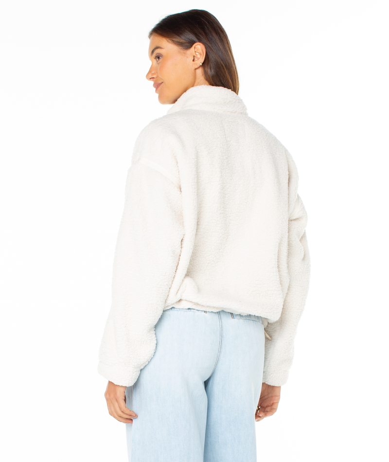 A person seen from behind, wearing a cozy, cream-colored high-neck Roxy Wurlie Fleece Jacket and light-wash blue jeans.