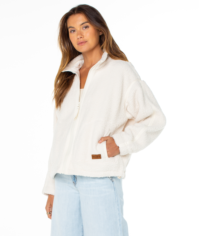A person wears a cream-colored Roxy Wurlie Fleece Jacket with a high collar and a small logo patch near the pocket for a coastal cool look.
