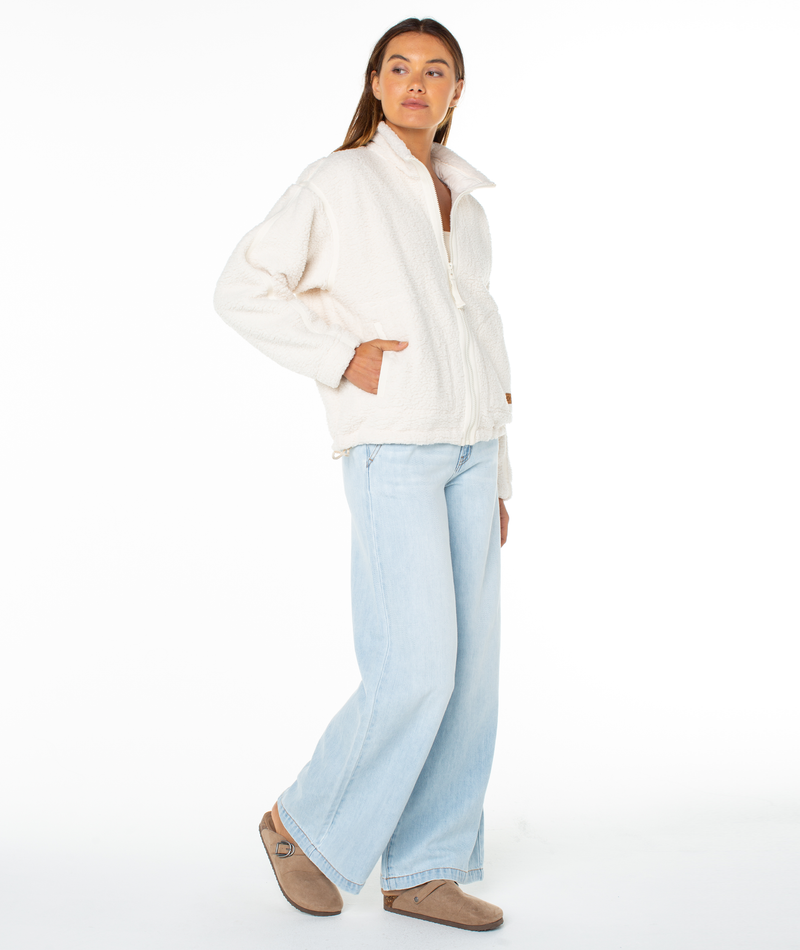 A person wearing a cozy Roxy Wurlie Fleece Jacket and light-wash wide-leg jeans.