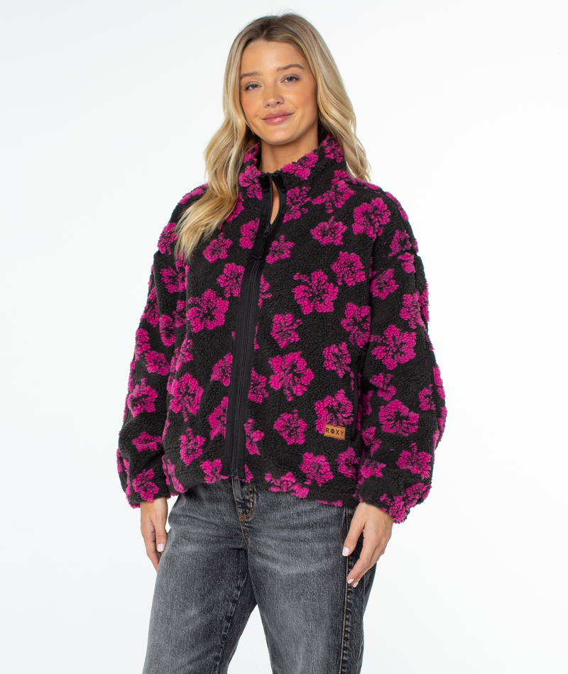 A woman wears a Roxy Wurlie Fleece Jacket in black, featuring a pink floral pattern and a zip-up front.