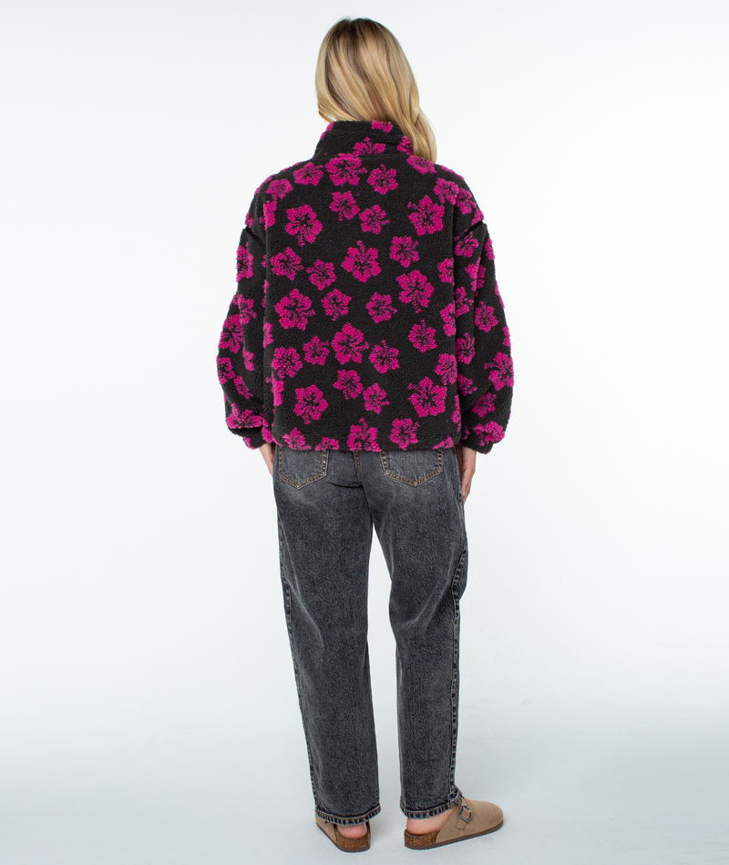 A person wearing a Roxy Wurlie Fleece Jacket in black with a pink floral print and dark grey jeans.