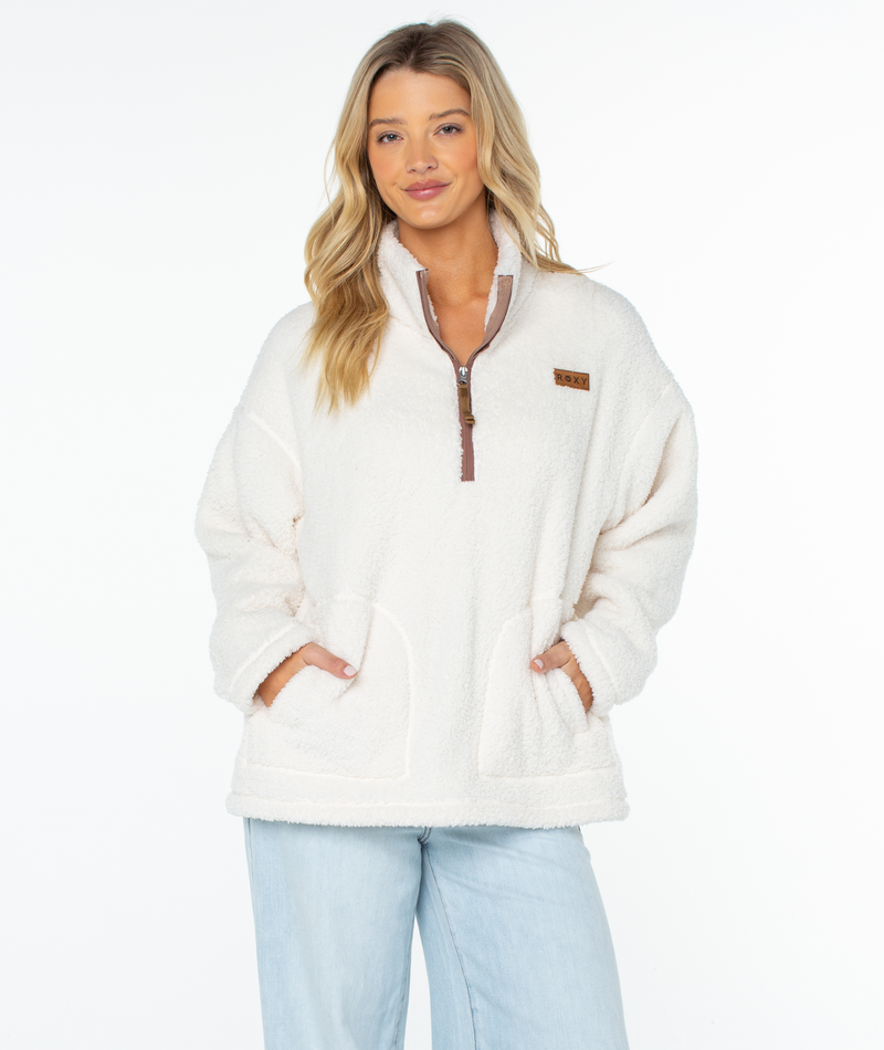 A woman wearing a Roxy Cozy Day Fleece Top in cream, featuring a long-sleeved fleece pullover with a cozy mock neck, quarter-zip collar, and oversized front pocket.
