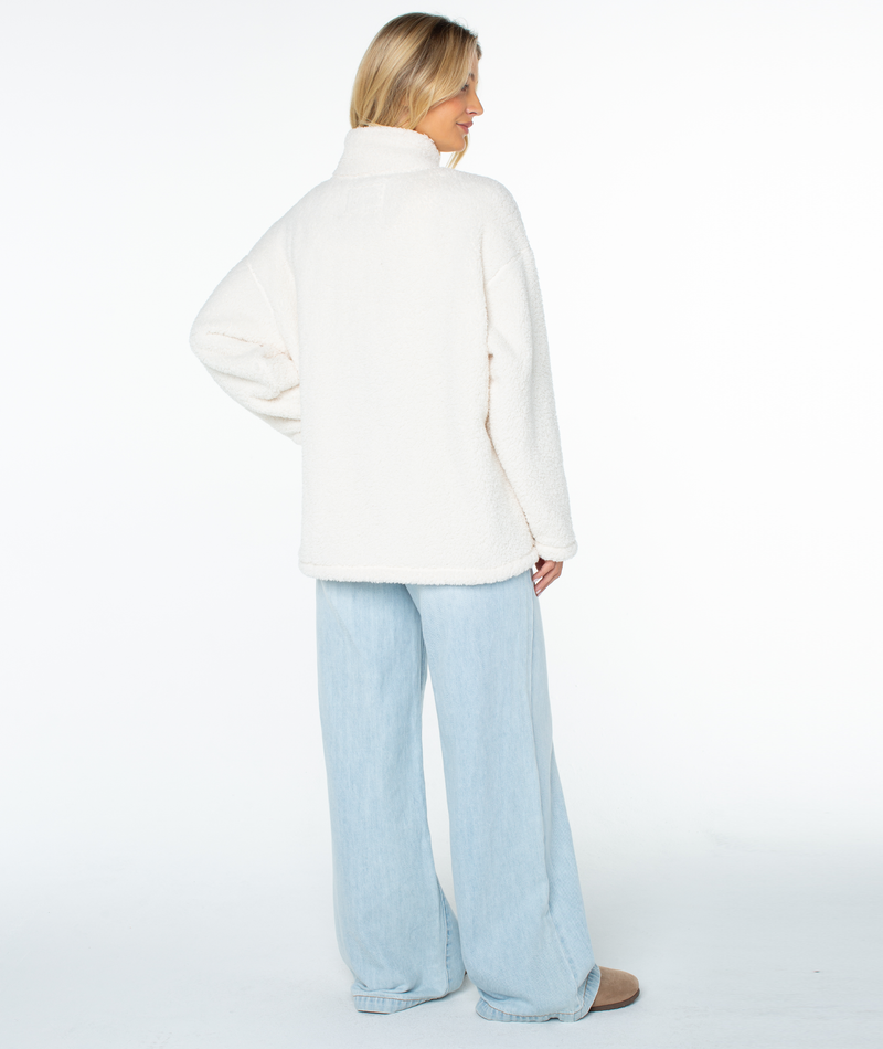 A person viewed from behind wearing a cream-colored Roxy Cozy Day Fleece Top and light-wash wide-leg jeans.