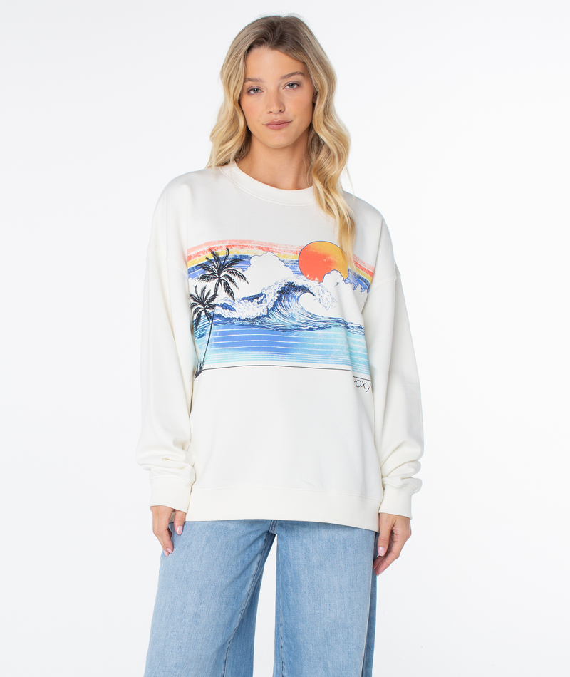 A woman wears an off-white Roxy Line Up Crew Top featuring a graphic of a tropical beach sunset with palm trees and a wave.