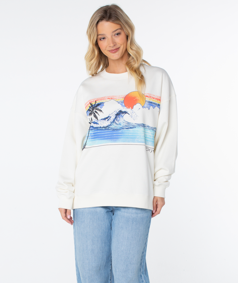 A woman wears an off-white Roxy Line Up Crew Top featuring a graphic of a sun, a large wave, and a palm tree.