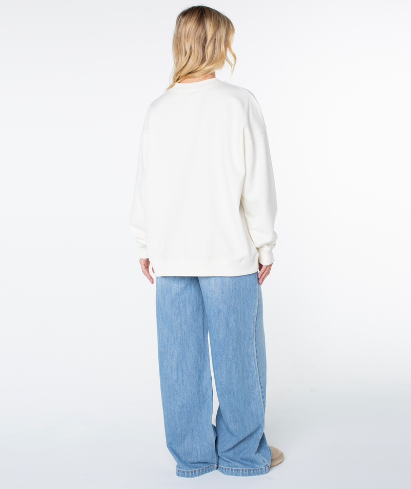 A person seen from behind wears a cream-colored Roxy Line Up Crew Top and loose-fitting blue jeans.