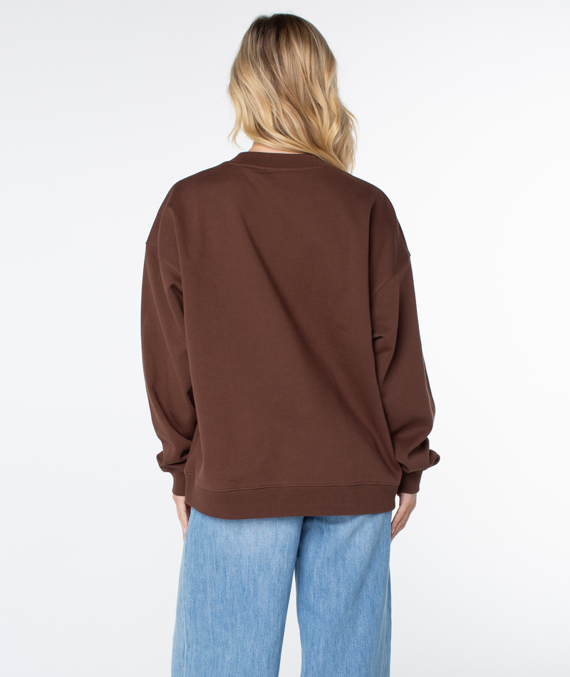 A person viewed from the back wearing a brown Roxy Line Up Crew Top and blue jeans.