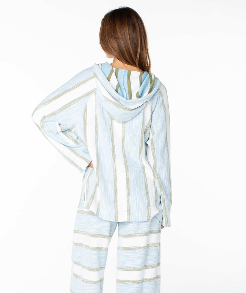 A person with long brown hair models the Wild And Free Top by Roxy—a loose, hooded lounge set in blue, white, and beige stripes—crafted from a soft cotton blend terry and shown from the back on a white background for effortless coastal vibes.
