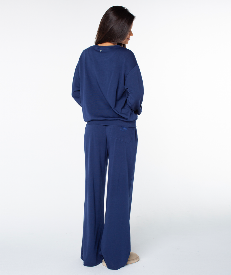 A person seen from behind, wearing a navy blue Roxy Surfing By Moonlight top with matching wide-leg trousers.