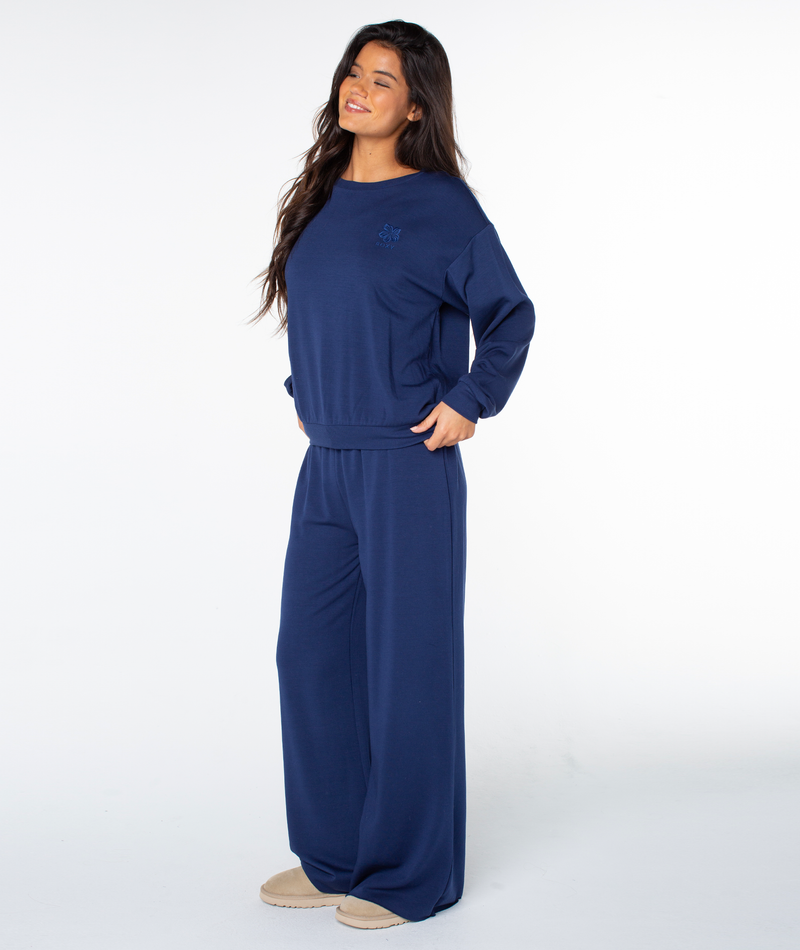 A woman wears a cozy, navy blue Roxy Surfing By Moonlight Top and matching wide-leg trousers.