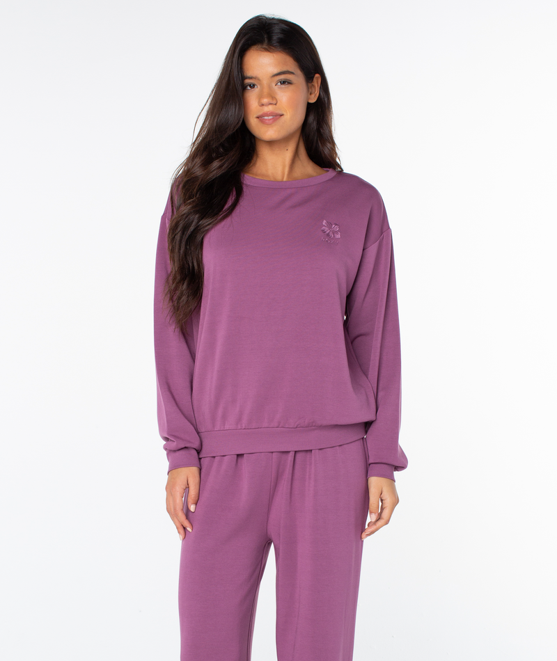 A person wearing a cozy, long-sleeved purple Roxy Surfing By Moonlight Top and matching lounge pants.