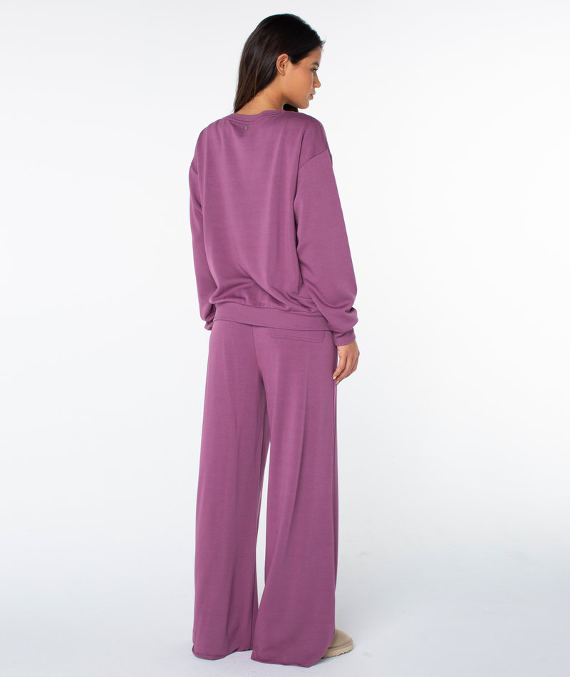 A person seen from behind, wearing a cozy, long-sleeved purple Surfing By Moonlight Top and matching wide-leg trousers.