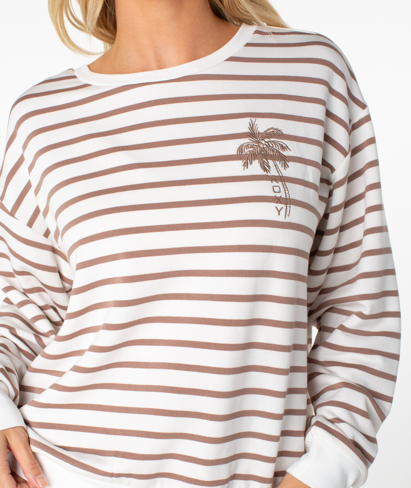 Wearing the Roxy Surfing By Moonlight Stripe Top—a long-sleeved white shirt with horizontal brown stripes and a palm tree JOY graphic—makes for the perfect cozy beach pullover.