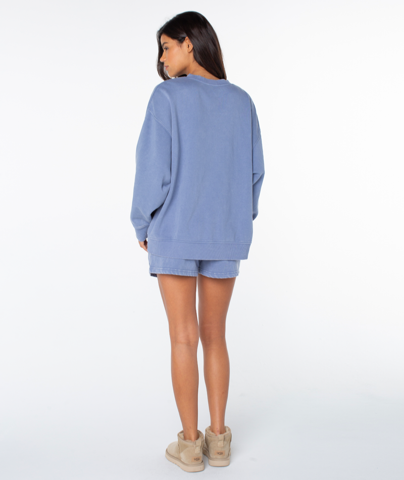 A woman stands facing away in a Roxy Hazy Daze Patch Top, matching blue shorts, and beige ankle boots against a white background.