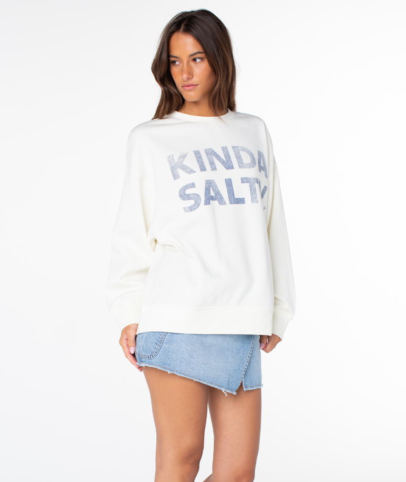A woman stands against a white background wearing the Roxy Morning Stroll Top in Coconut Milk Kinda Salty and a short, asymmetrical denim skirt for an effortless, everyday style.