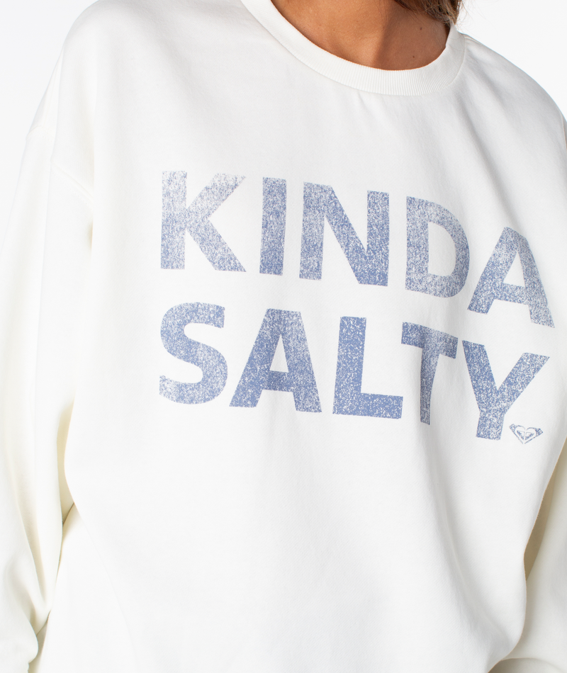 A person wearing the Roxy Morning Stroll Top—a cozy cotton crewneck sweatshirt with KINDA SALTY printed in large, sparkly blue letters—your new wear-everywhere favorite.