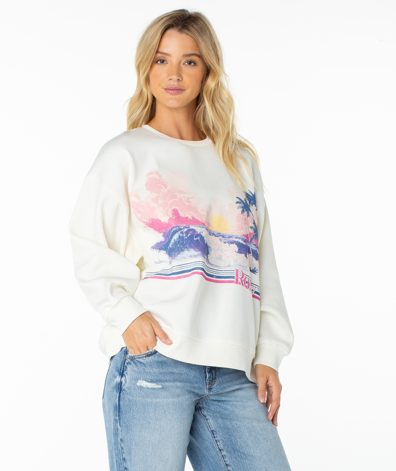 A person wearing a coconut milk salt sunrise Roxy Morning Stroll Top, an off-white crewneck sweatshirt featuring a graphic of a sunset over the ocean with palm trees.