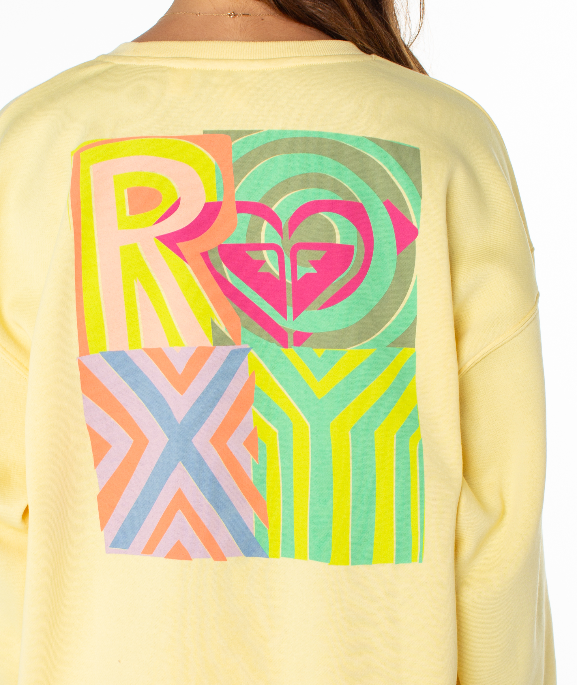 A person wearing the Roxy Morning Stroll Top, a yellow crewneck sweatshirt with a vibrant geometric graphic on the back, bold ROXY lettering, and a heart-shaped logo at the center—a perfect summer staple.