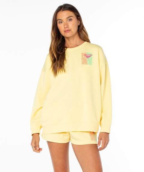 A woman with long hair poses against a white background in the Roxy Morning Stroll Top, a loose-fitting pale yellow crewneck sweatshirt featuring colorful geometric graphics—perfect as a cozy summer staple.