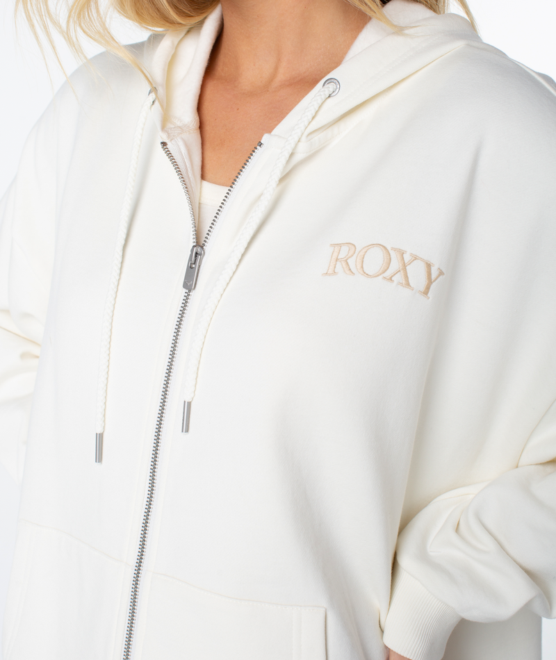 A woman wears the Roxy Line Up Zip, a white cotton-blend hoodie with beige ROXY embroidery, drawstrings, and a cozy, relaxed fit for casual style.