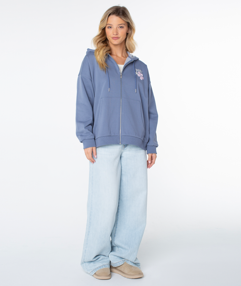 A woman faces forward in a casual look, wearing the Roxy Line Up Zip hoodie in Wild Wind Stitched Sunset, light-wash wide-leg jeans, and beige shoes against a plain white background.