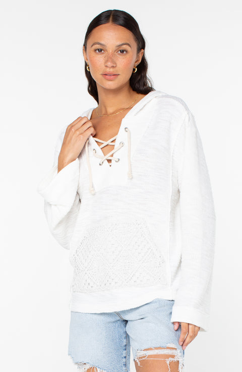 A woman wears the Roxy Pearling Poncho 3 white lace-up hoodie with front pocket and light blue distressed denim shorts, standing against a plain white background and looking at the camera.