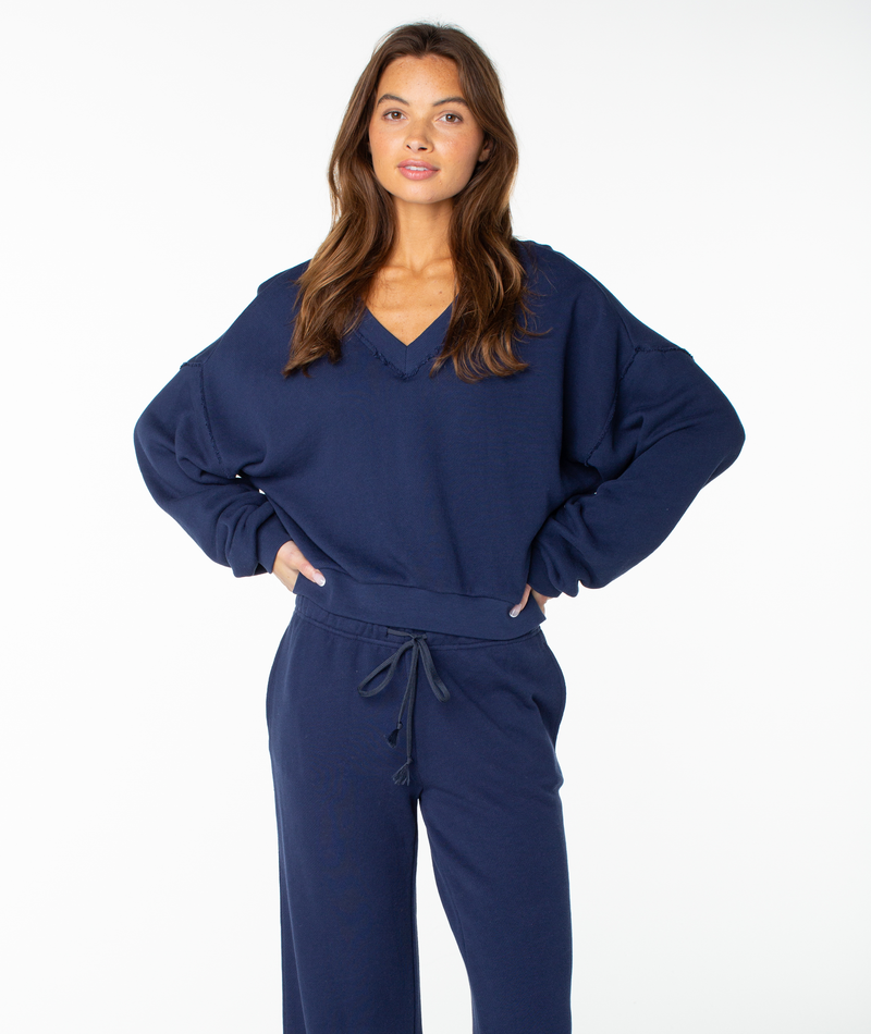 A woman stands with hands on her hips, wearing the Roxy Dream Thing Top in Naval Academy Solid, paired with matching drawstring cropped pants, against a white background.