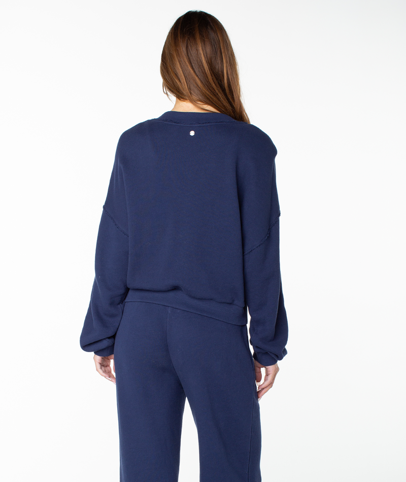 A person with long brown hair is shown from behind, wearing the Roxy Dream Thing Top, a navy blue cotton crewneck sweatshirt, against a plain white background.