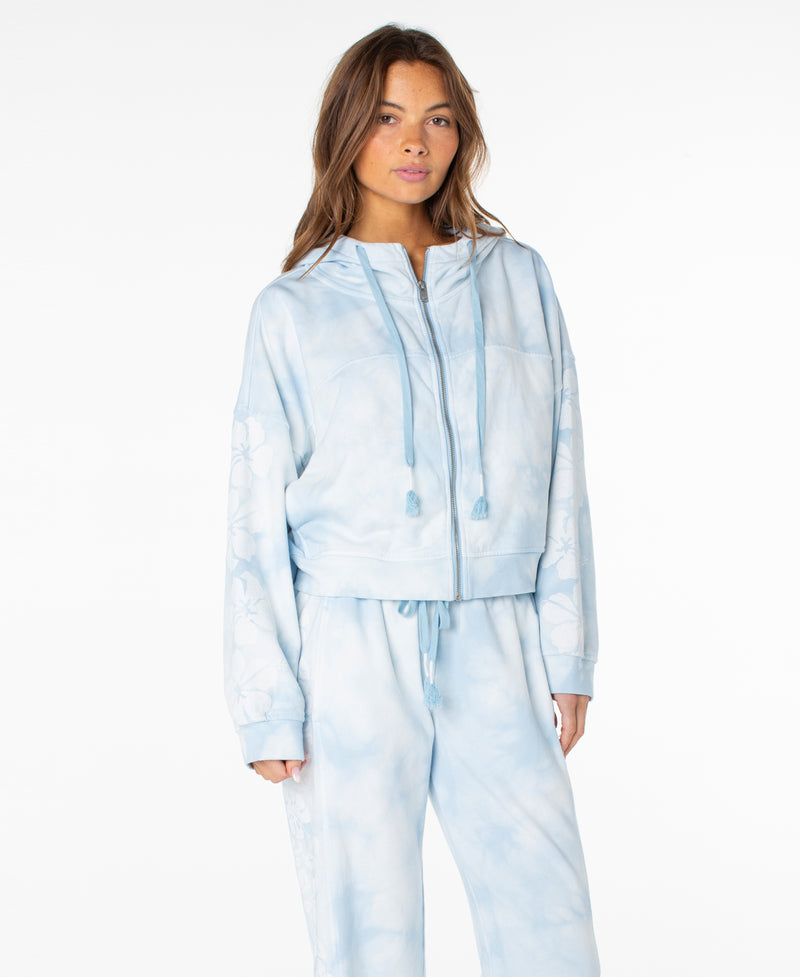 A woman wearing the Roxy Fringing Reefs Top in Cerulean Tie Dye stands against a plain white background, showcasing comfortable loungewear style.