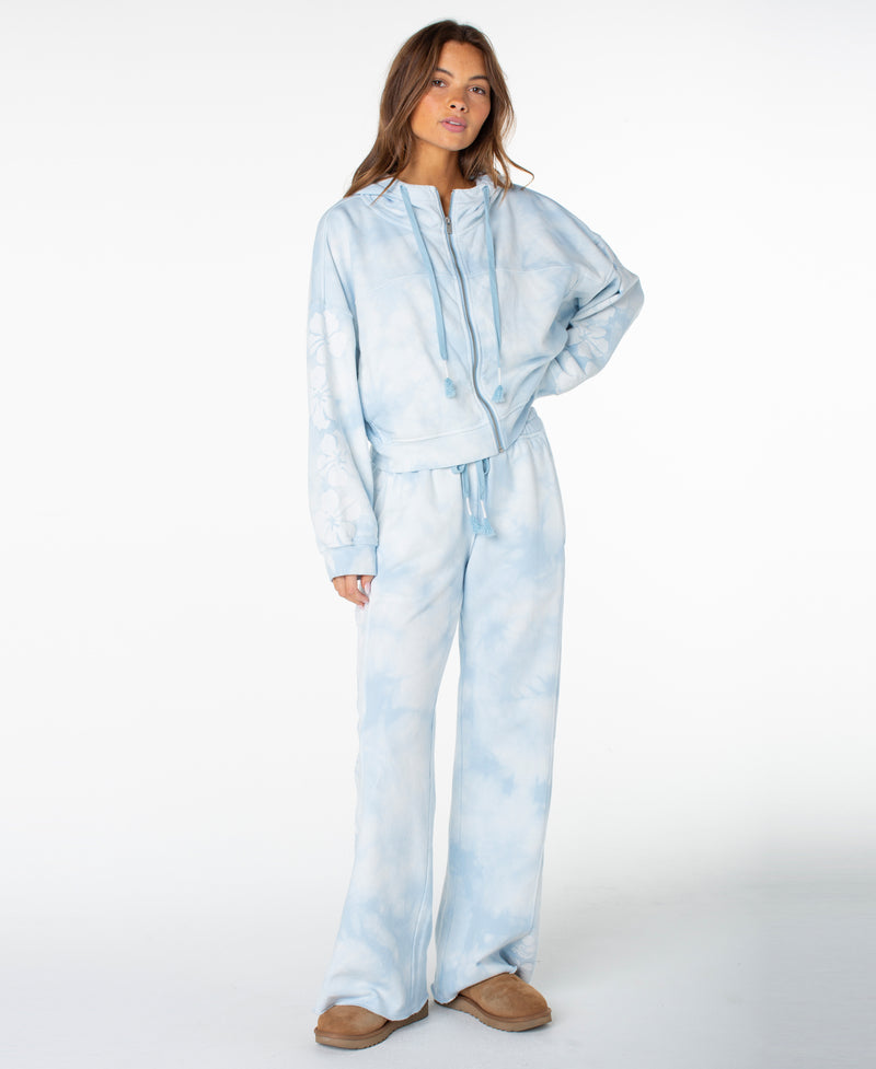 A woman stands in a relaxed pose wearing the Roxy Fringing Reefs Top paired with wide-leg pants and tan slippers against a plain white background.