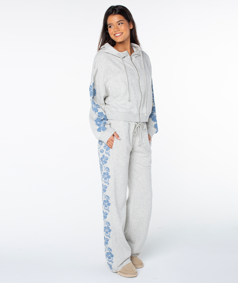 Woman smiles in the Fringing Reefs Top by Roxy in Heather Grey Fringing Reefs, hands in pockets, wearing cozy loungewear against a white background.