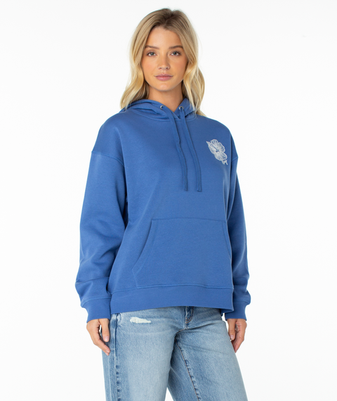 A woman with blonde hair wears the Roxy Wailea Hoodie in Dutch Blue Stitched Hibiscus, featuring an ultra-soft fabric and a small white graphic on the left chest, paired with light blue ripped jeans as she stands against a plain white background.