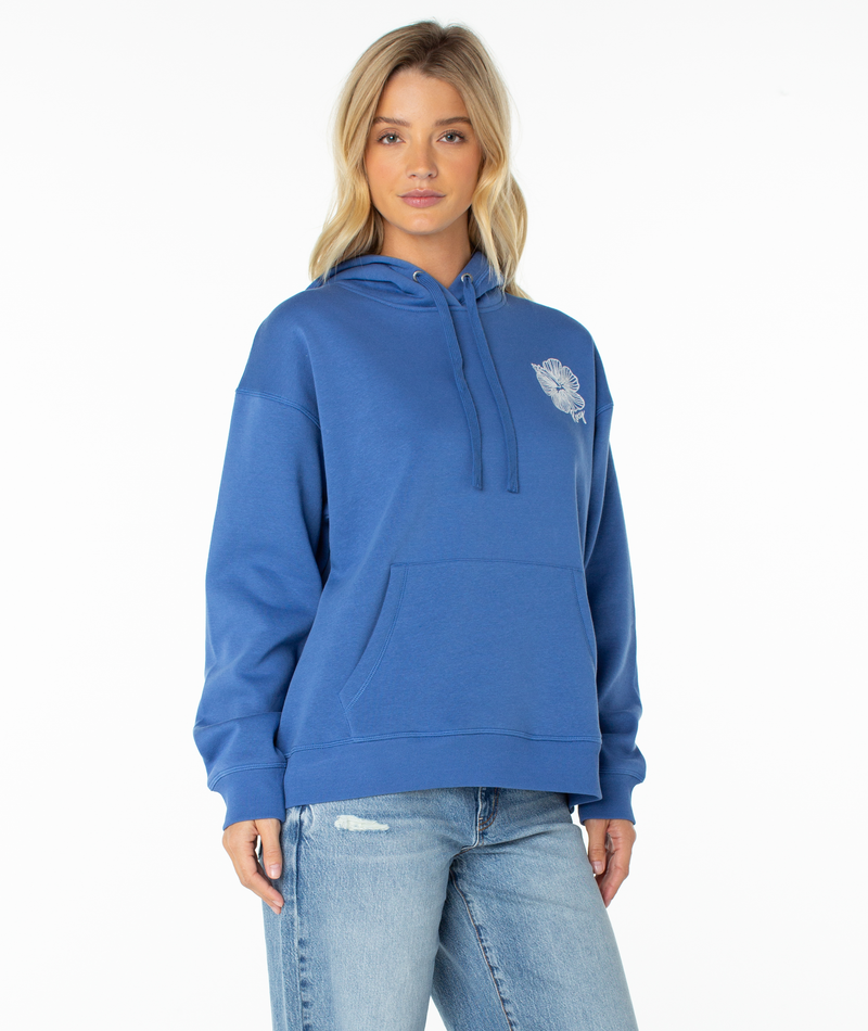 A woman with blonde hair wears the Roxy Wailea Hoodie in Dutch Blue Stitched Hibiscus, featuring an ultra-soft fabric and a small white graphic on the left chest, paired with light blue ripped jeans as she stands against a plain white background.