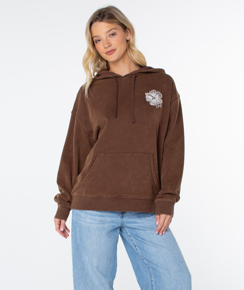 Woman in the ultra-soft Roxy Wailea Hoodie, featuring a floral design on the left chest, paired with light blue jeans and standing against a plain white background.