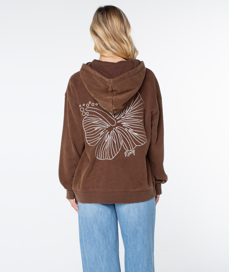 A person with long blonde hair wears the ultra-soft Wailea Hoodie by Roxy, with a bold white floral design on the back, styled with light blue jeans against a plain white background.