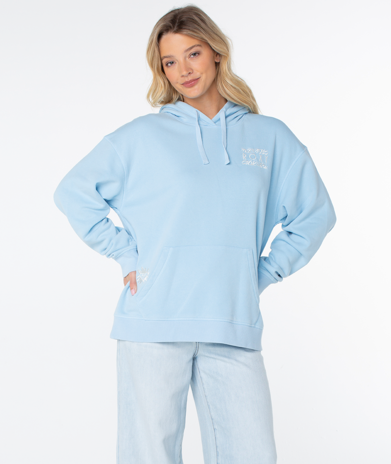 A woman models the Roxy Wailea Hoodie in light blue with light-wash jeans, standing hands on hips and smiling softly against a white background.