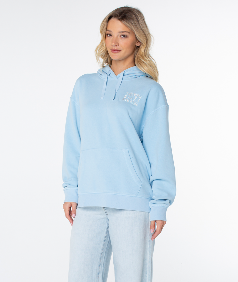 A woman with long blonde hair wears the Roxy Wailea Hoodie in light blue and light jeans, standing against a plain white background and smiling slightly.