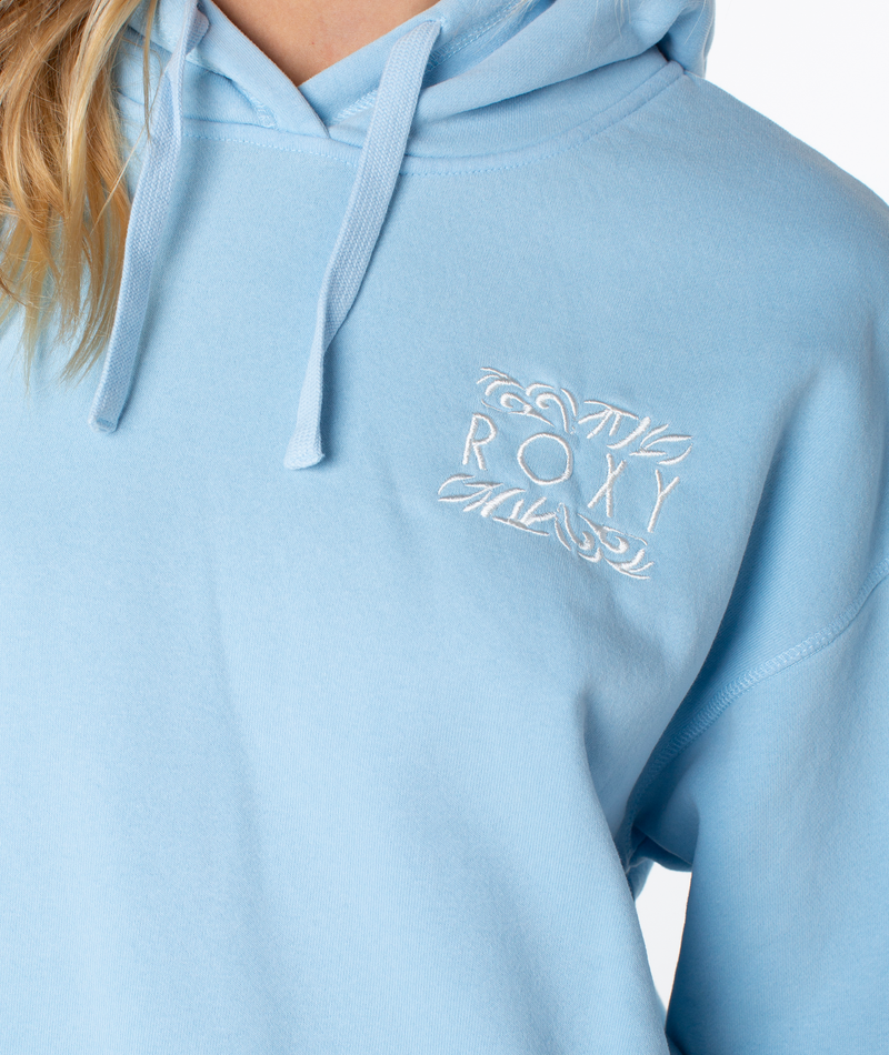 Someone wears the ultra-soft Wailea Hoodie in light blue by Roxy, featuring white ROXY embroidery on the chest and decorative stitching. Only part of their face and hair is shown.