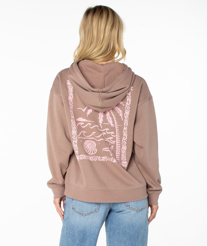 A person with blonde hair, seen from behind, is wearing a slouchy, ultra-soft brown Wailea Hoodie by Roxy and blue jeans. The hoodie showcases a light pink beach scene graphic with palms, waves, and a shell on the back.