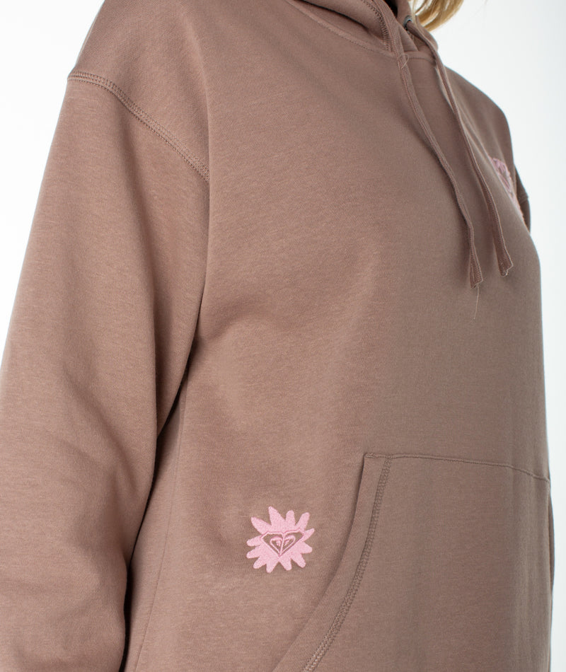 A person wearing the Roxy Wailea Hoodie in mauve, which features a kangaroo pocket and a small pink flower patch near the pocket. The photo is cropped just below the shoulders.
