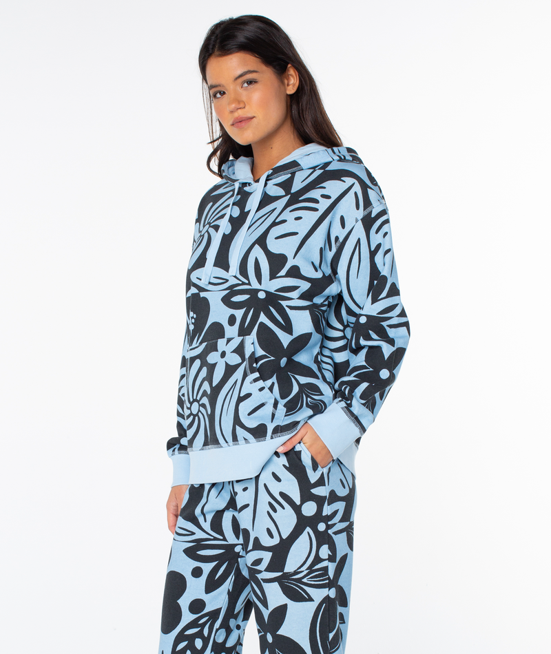 A model wearing a Roxy Maile Printed Hoodie in light blue with a black tropical leaf print and a matching drawstring hood.