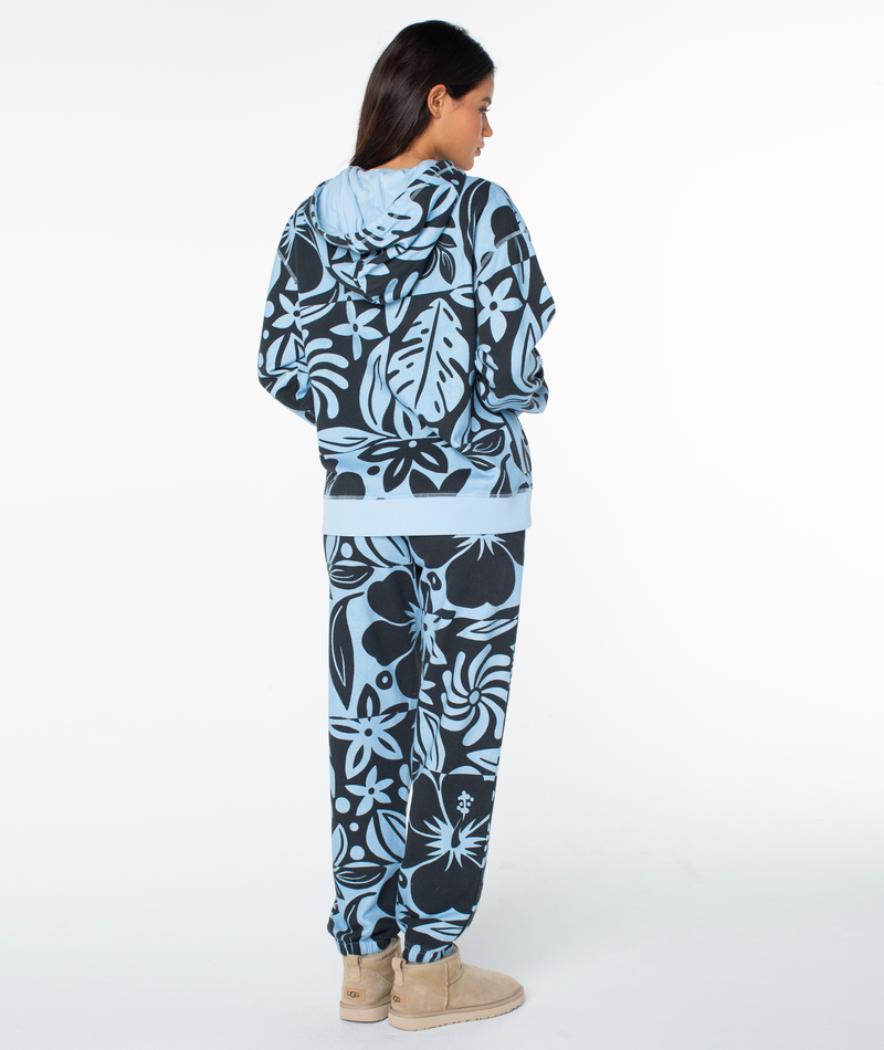 A person seen from the back wearing a Roxy Maile Printed Hoodie and matching sweatpants in a light blue and black floral print, paired with tan ankle boots.